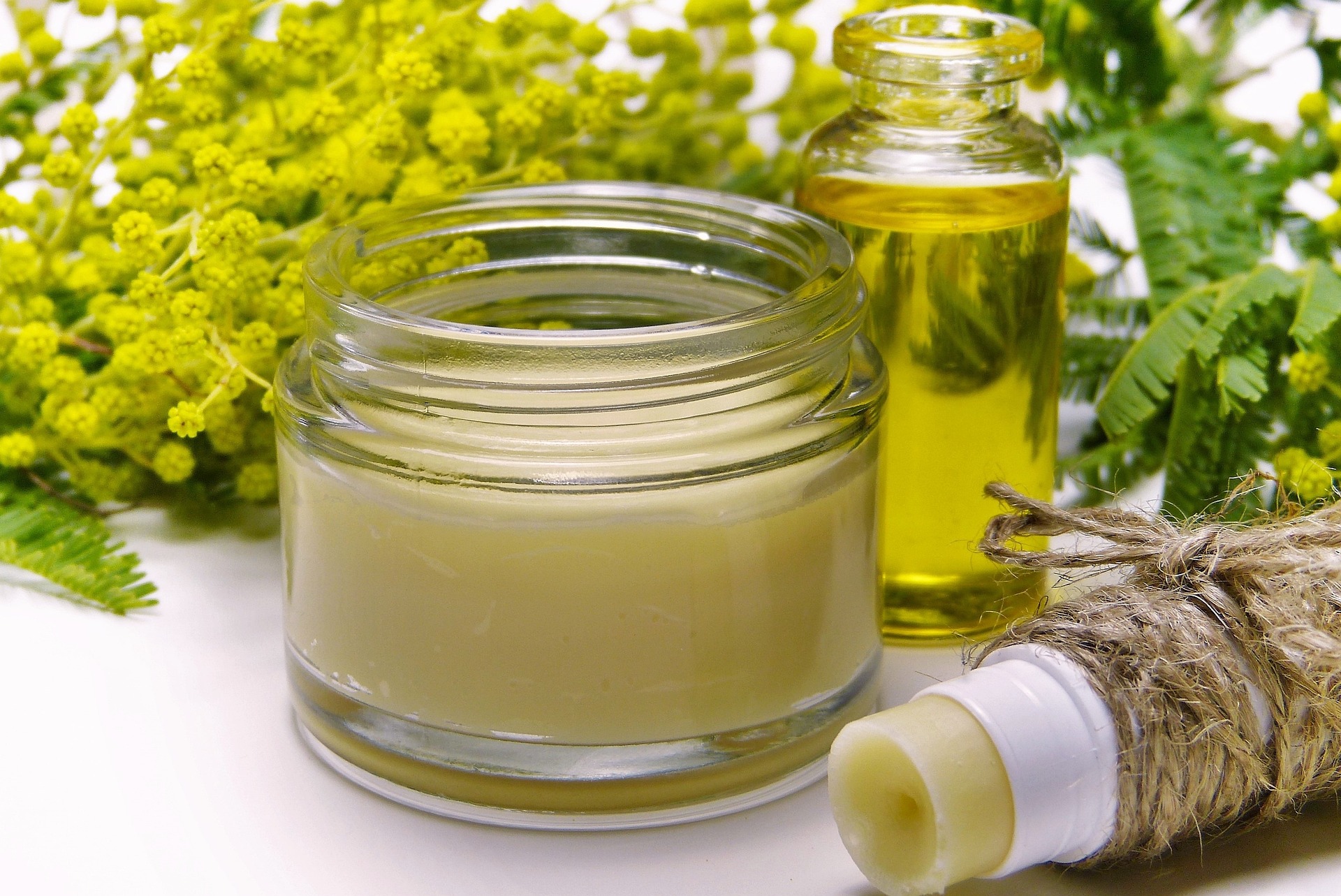 small jar of salve surrounded by yellow flowers, a jar of oil, and an open chapstick