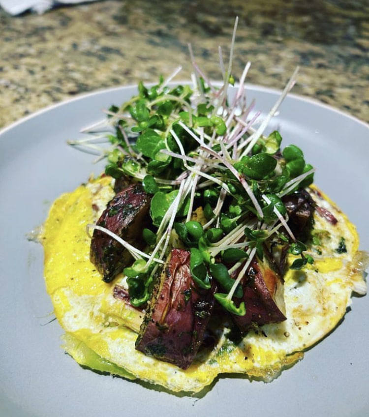 small omelet topped with herb roasted potatoes and microgreens