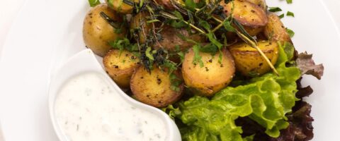 roasted gold potatoes topped with herbs on a bed of lettuce. Adjacent is a bowl of creamy herb dressing