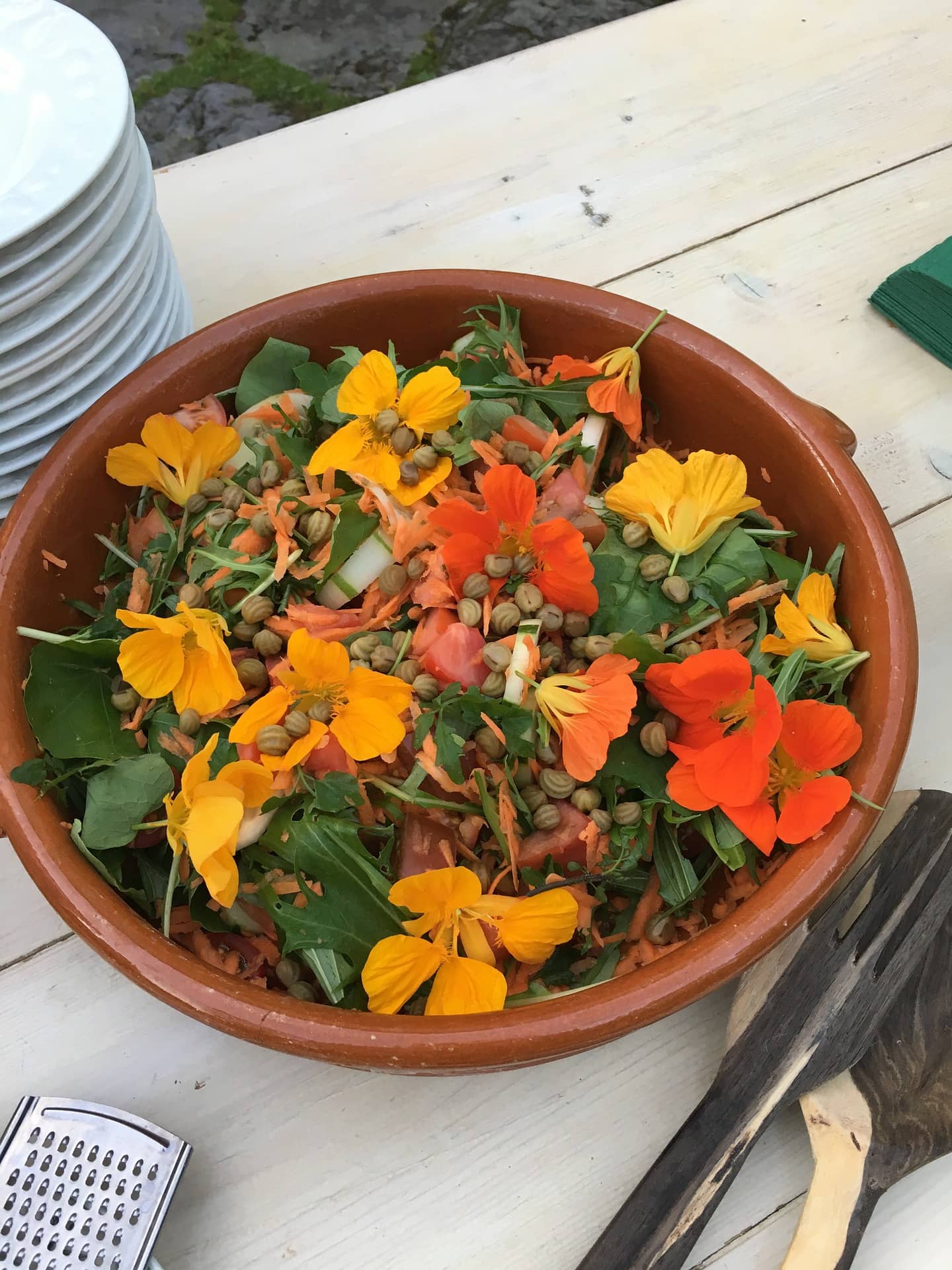 a brown bowl with chopped spinach, lentils, cucumber, tomato, and nasturtium (orange and yellow flowers) salad