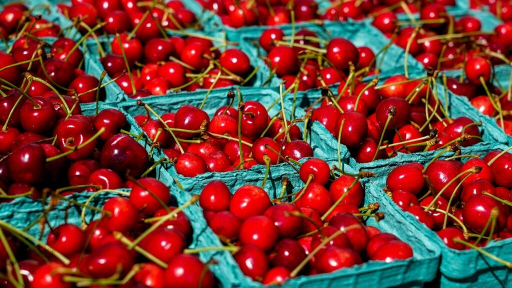 Vibrant red cherries in green cartons at a sunny farmers market. Fresh and ripe.