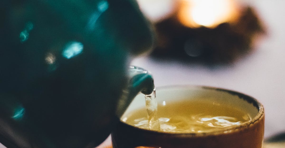 Warm close-up image of tea being poured into a teacup with blurred background ambiance.